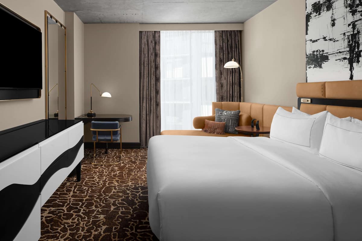 Een hotelkamer met een groot bed, een bureau met stoel, een televisie en een groot raam met gordijnen.