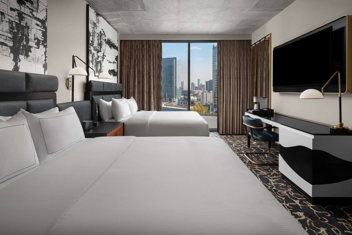 Een hotelkamer met twee bedden, een bureau, een televisie en een groot raam met uitzicht op de stad.