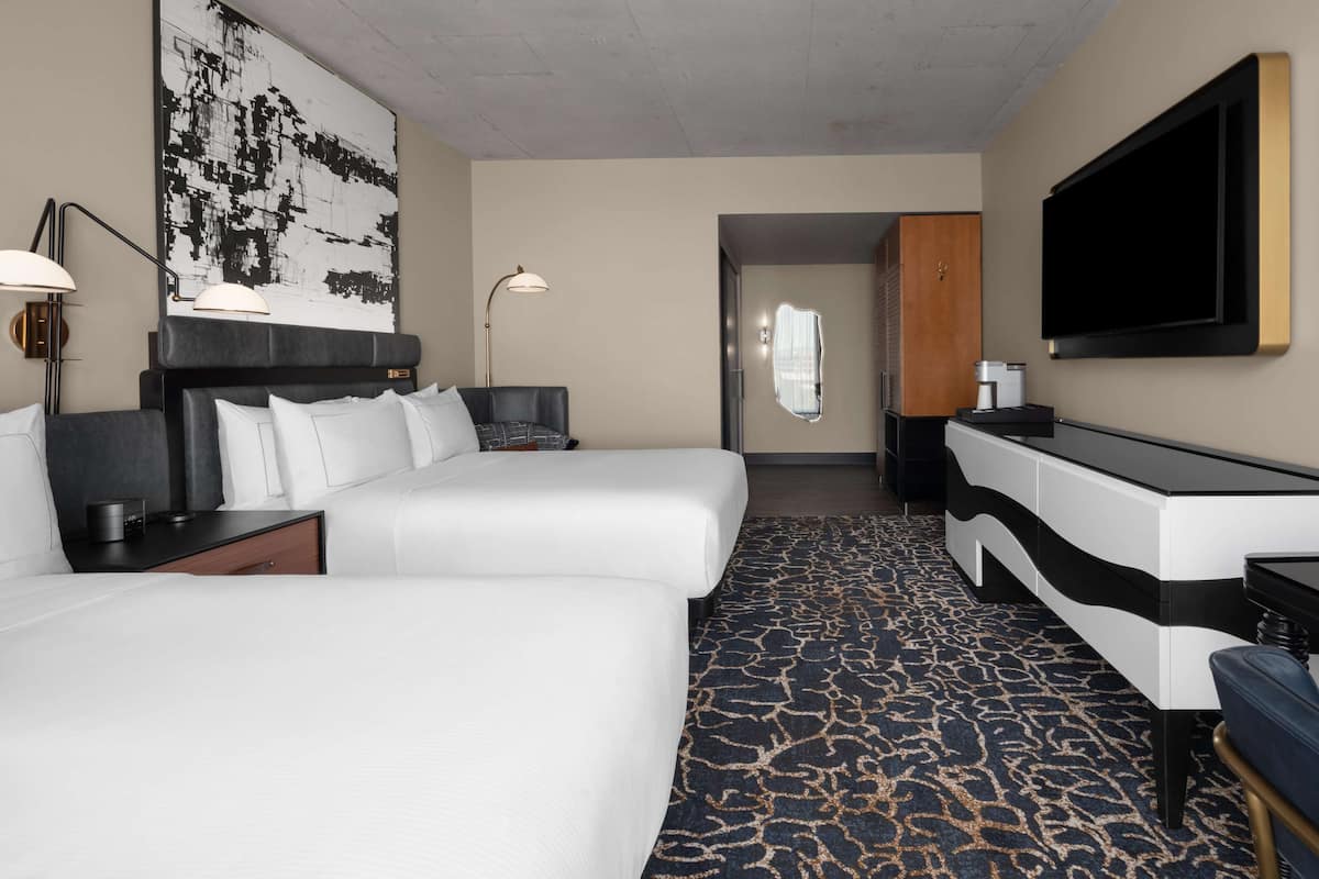 Een hotelkamer met twee bedden, een bureau, een flatscreen televisie, een groot abstract schilderij en een kamerbreed tapijt met dessin.