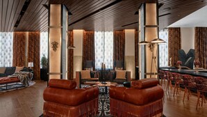 Een ruime woonkamer met lederen fauteuils, een centrale salontafel en een bar met rode bekleding.
