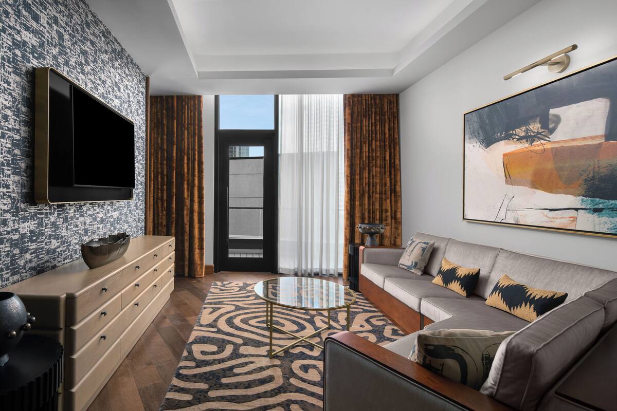 Een moderne woonkamer met een flatscreen televisie, een bank met gekleurde kussens, een salontafel en een groot abstract schilderij.