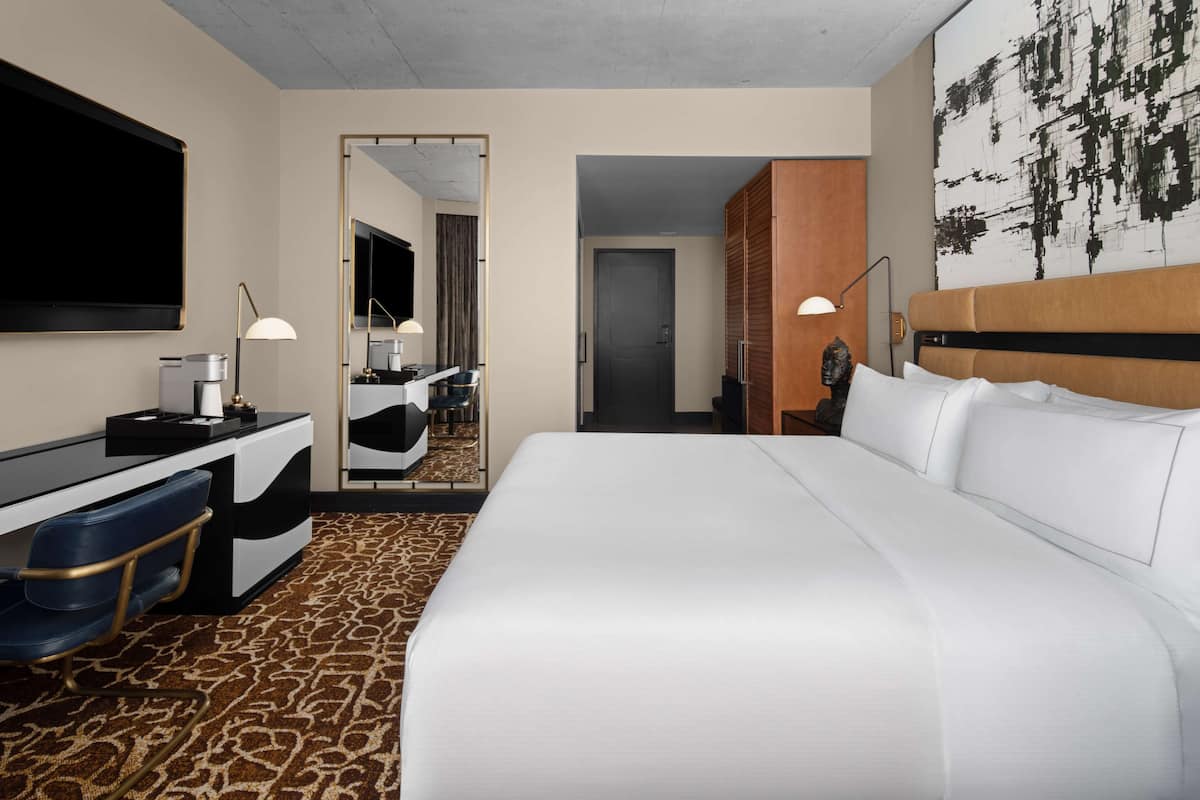 Een hotelkamer met een groot bed, een bureau met stoel, een spiegel en een televisie aan de muur.