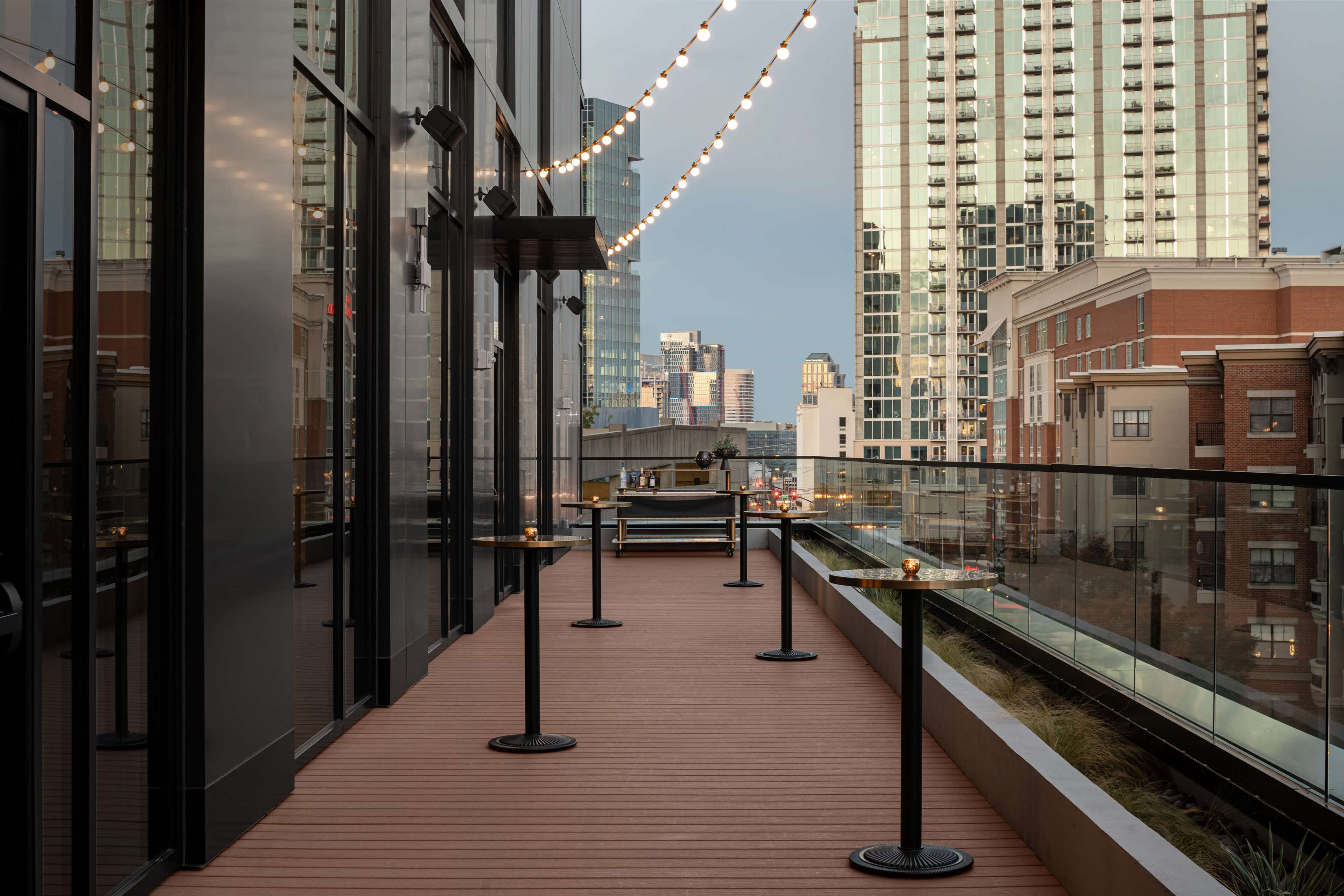 A modern outdoor terrace with a wooden floor, glass railings, and string lights.