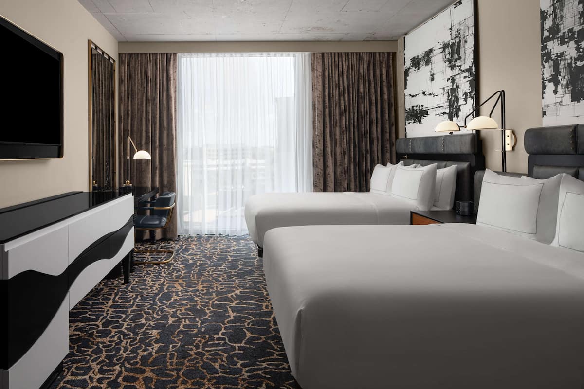 Een hotelkamer met twee bedden, een televisie, een bureau en een groot raam met gordijnen.