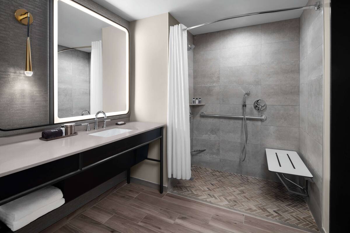 Een moderne badkamer met een grote spiegel, twee wastafels, een douche met glazen deur en een visgraatvloer.