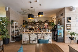 Enjoy a warm atmosphere in our cozy café, featuring a rustic bar counter, shelves, and a large artwork.