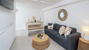 A modern living room with a grey sofa, a round wooden coffee table, and a white console table with decorative items.