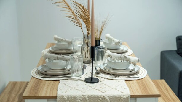 A dining table set with plates, bowls, glasses, and a vase with dried plants.