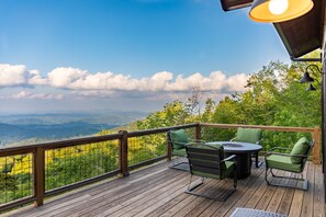 A wooden deck with outdoor furniture, a table, and chairs, overlooking a mountainous landscape.