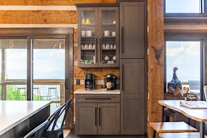 A kitchen with dark cabinets, a coffee maker, and a view of the outdoors.