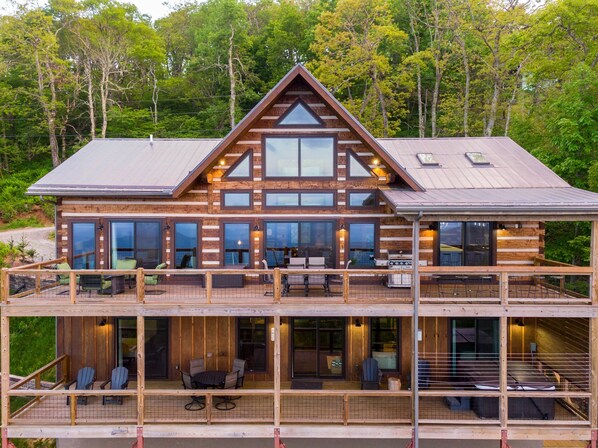 A two-story log cabin with a balcony, large windows, and a deck with outdoor seating.