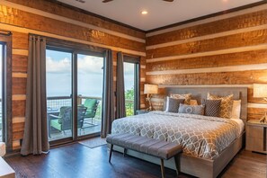 A bedroom with a large bed, a bench, a nightstand, and a view of the outdoors through a sliding glass door.