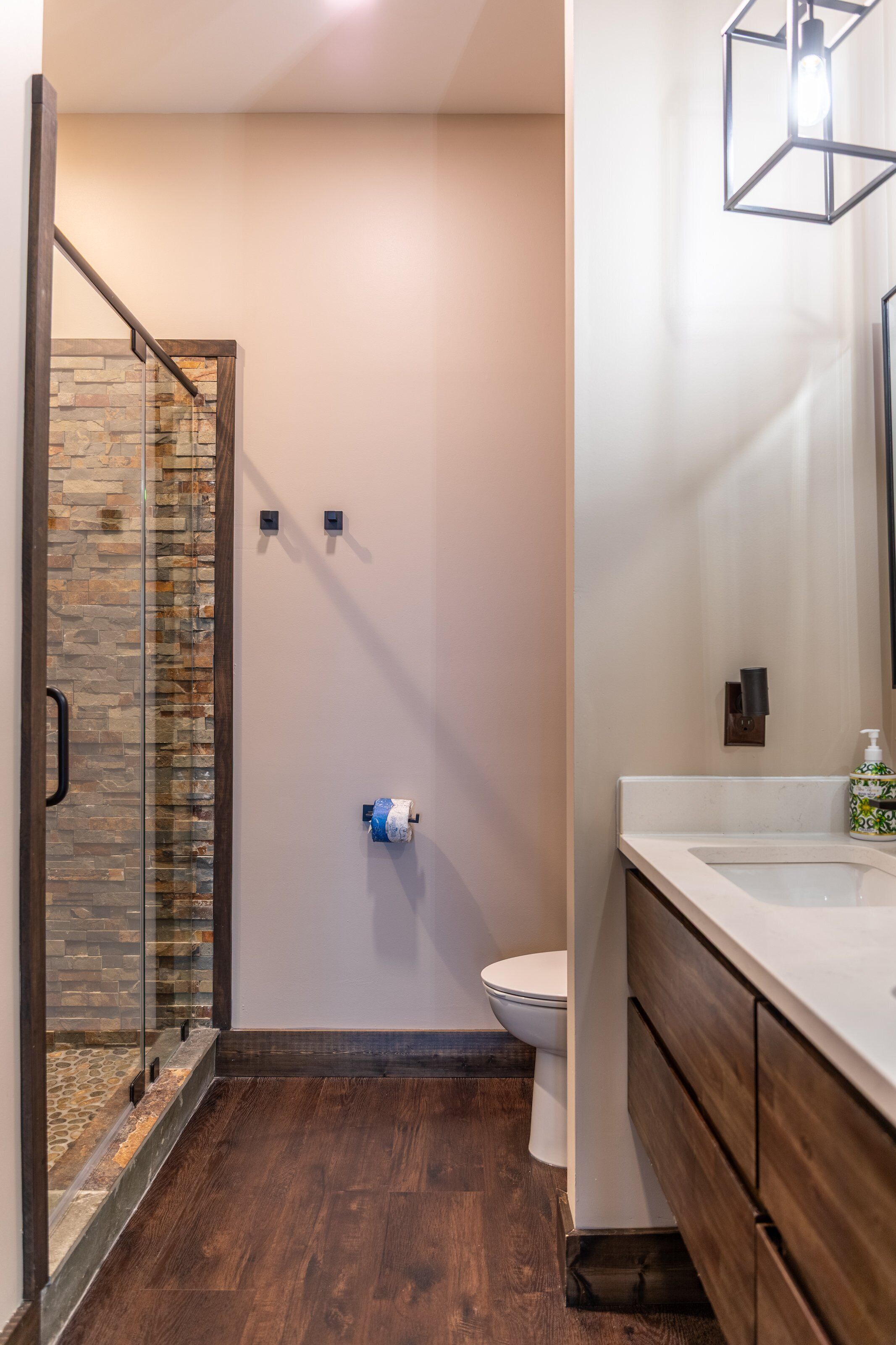 A bathroom with a glass shower enclosure, a toilet, and a vanity with a mirror.