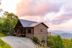 A log cabin with a metal roof, wooden exterior, and a gravel driveway.