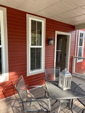 Une façade rouge avec des éléments décoratifs blancs, un patio couvert avec des chaises et une table en métal, et une lanterne.