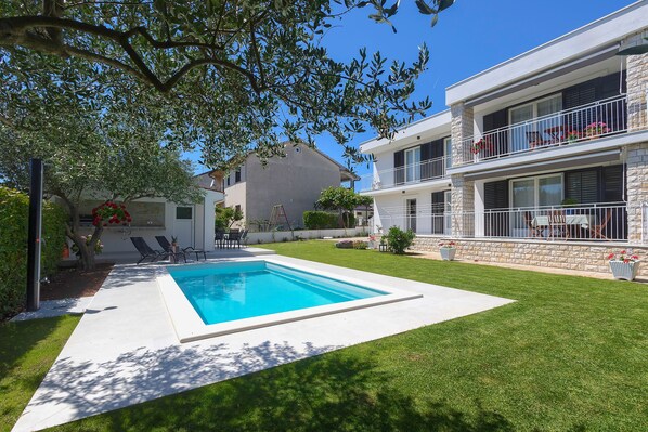 A residential property with a swimming pool, a well-maintained lawn, and a two-story building with balconies.