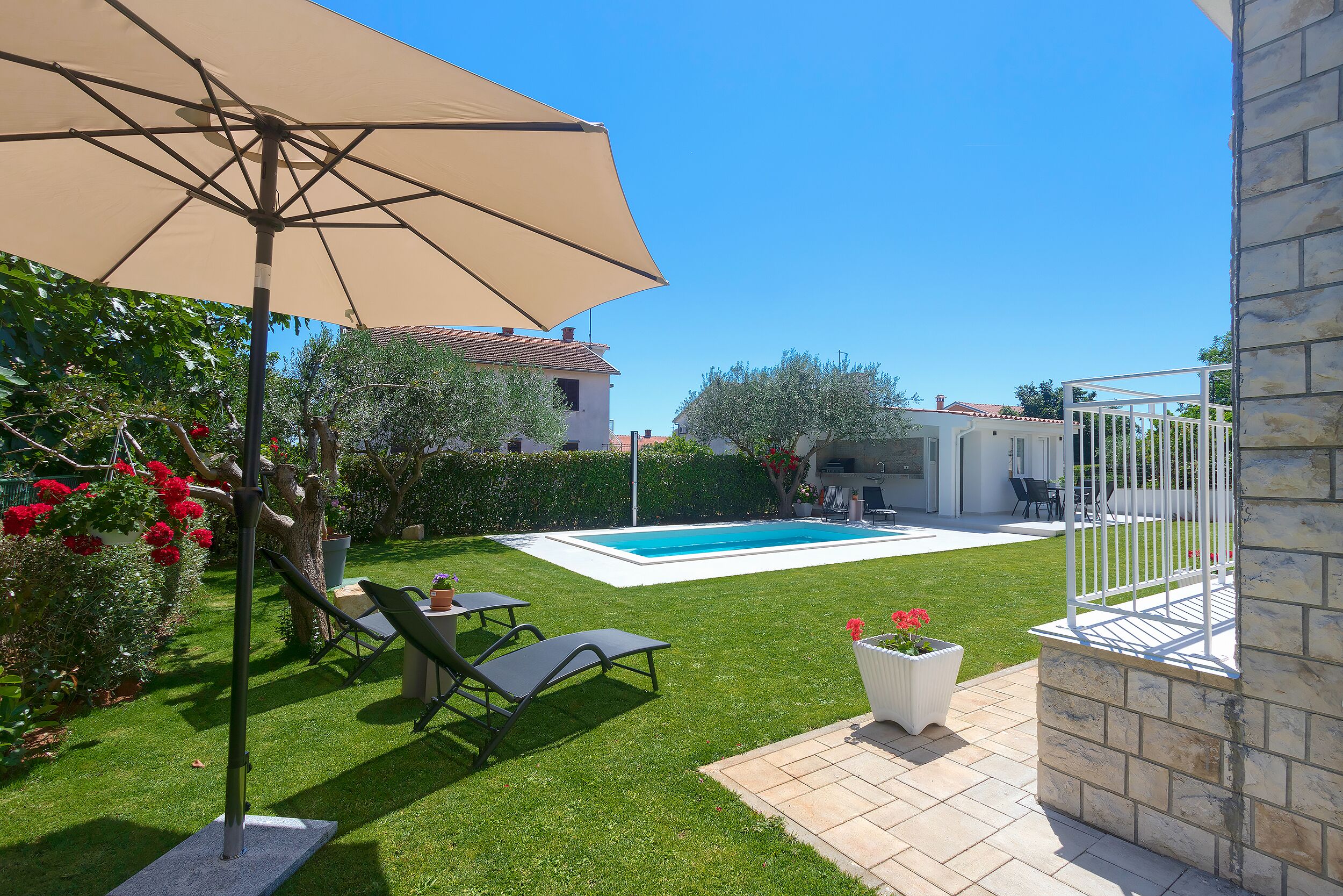 A backyard with a swimming pool, a pergola with a beige canopy, and a stone wall.
