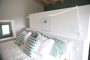 A bedroom with a bed, pillows, a bedside table, a lamp, and a window.