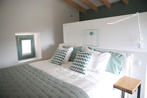 A bedroom with a bed, pillows, a bedside table, a window, and a wall-mounted light fixture.