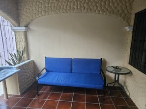 A blue sofa in a corner with a stone wall and a small table with a plant.