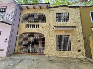 Edificio de dos pisos con ventanas protegidas por rejas y un balcón.