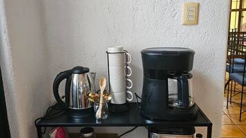 A kitchen counter with a coffee maker, a kettle, a jar of sugar, and a small container of spices.