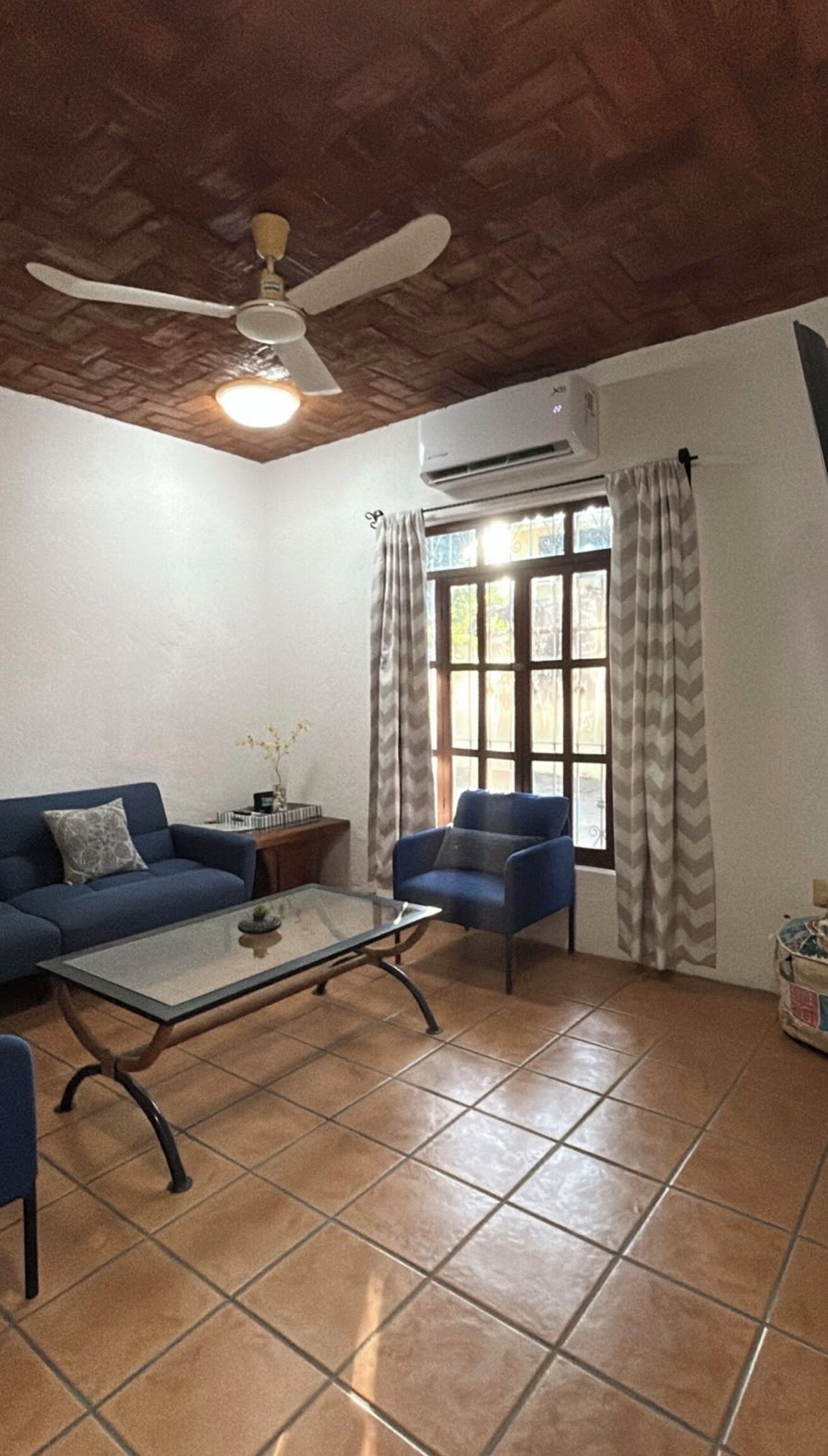 A living room with a ceiling fan, a sofa, a chair, a coffee table, and a window with curtains.