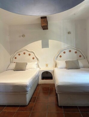 Habitación con dos camas, cada una con cabecera, un pequeño estante de madera y una lámpara de pared.