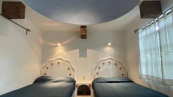 A room with two beds, a curved ceiling, and a window with curtains.