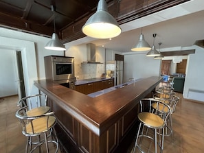 Une cuisine moderne dotée d’un îlot central, de tabourets de bar, d’appareils électroménagers en acier inoxydable et de luminaires suspendus.