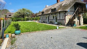 Une maison traditionnelle à colombages, avec un toit de chaume, une pelouse bien entretenue et une allée gravillonnée.
