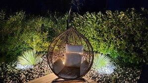Un fauteuil suspendu avec des coussins, installé dans un jardin.