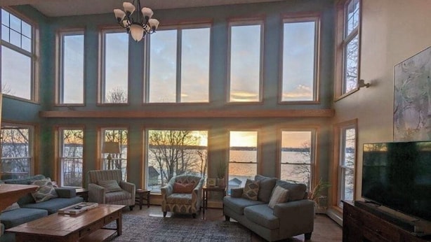 A spacious living room with large windows, a wooden coffee table, a sofa, and a television. - 200' of private waterfront, hot tub & kayaks (Cayuga)