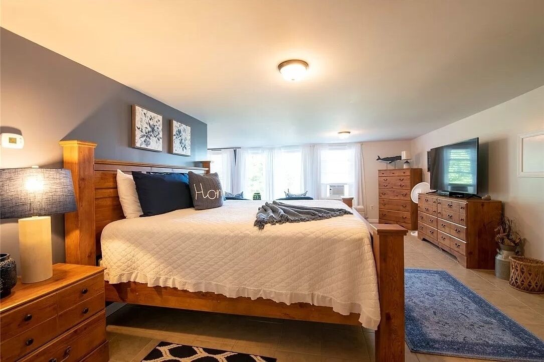 A bedroom with a bed, bedside tables, a dresser, a television, and artwork on the walls.