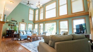 A spacious living room with a high ceiling, large windows, and a ceiling fan. - 200' of private waterfront, hot tub & kayaks (Cayuga)
