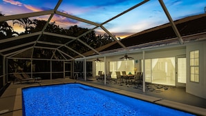 An indoor swimming pool with a glass ceiling, lounge chairs, and a patio area with tables and chairs.