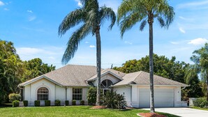 A single-story house with a garage, surrounded by a well-maintained lawn and palm trees.