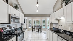 A modern kitchen with white cabinetry, a black countertop, and a dining area with a view of a pool.
