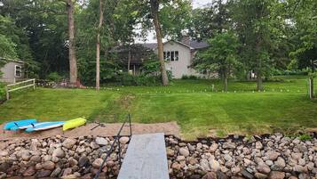 A backyard with a grassy lawn, a wooden deck, and a small pond with a blue kayak and yellow canoe.