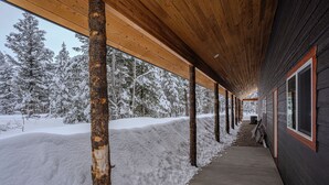 Un pasillo cubierto de madera que conduce a un edificio con grandes ventanales, rodeado de árboles cubiertos de nieve.