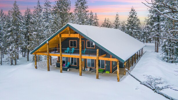 Una cabaña de troncos con un porche cubierto, rodeada de árboles cubiertos de nieve.