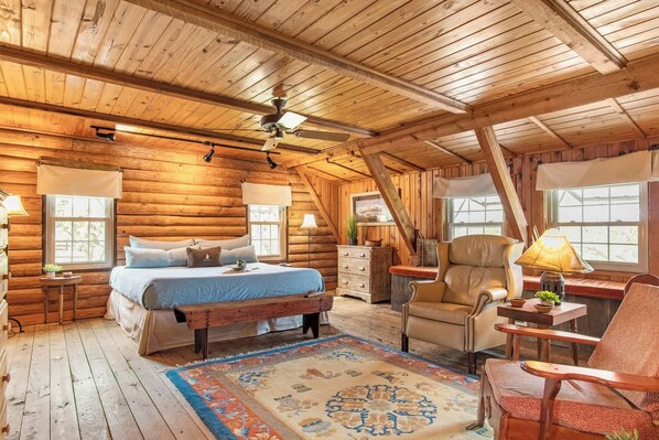 Ein Schlafzimmer in einer Blockhütte mit einem Bett, einem Schreibtisch, einem Stuhl und einem Fenster.
