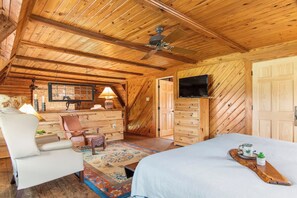 Una habitación acogedora con una cama, una silla, un escritorio, un televisor y un ventilador de techo.