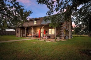 A log cabin with a porch, a covered outdoor seating area, and a stone chimney.
