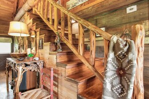 A wooden staircase with a handrail, a table with a lamp, and a woven chair. - Doe Creek Ranch | 2BR Cabin with Horse Amenities (Bandera)