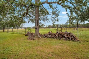 A tree with a black post and a stack of logs in a fenced field. - Doe Creek Ranch | 2BR Cabin with Horse Amenities (Bandera)