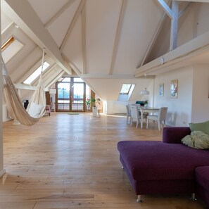 A spacious loft with high ceilings, a hammock, a purple sofa, and a dining area with natural light.