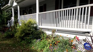A porch with a white railing, surrounded by a variety of plants and flowers. - The Jahmtons Guest Room (Ridge)