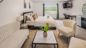 A modern hotel room with a bed, sofa, armchair, desk, TV, and a window with curtains. - Beautiful modern villa with pool suana hot tub... (Clintondale)