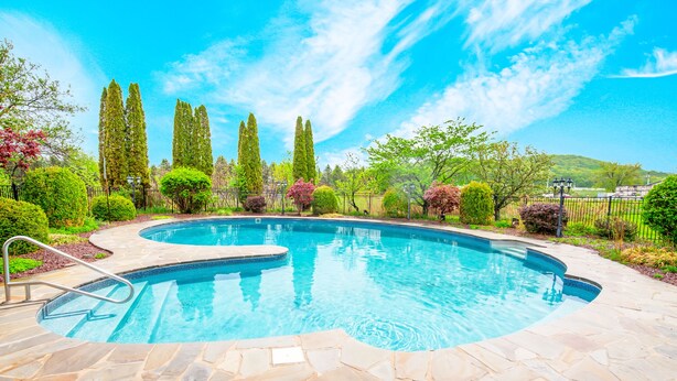 A swimming pool with stone tiles, surrounded by greenery and tall trees. - Beautiful modern villa with pool suana hot tub... (Clintondale)